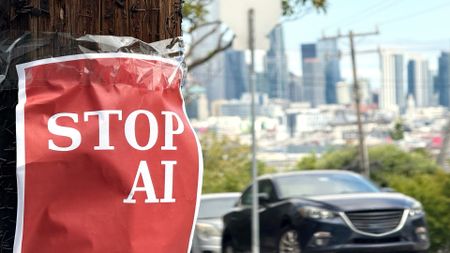 Red protest poster with STOP AI message taped to wooden pole beside urban street with blurred downtown skyline