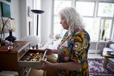 Senior woman wearing colorful at home opening drawer with precious cutlery