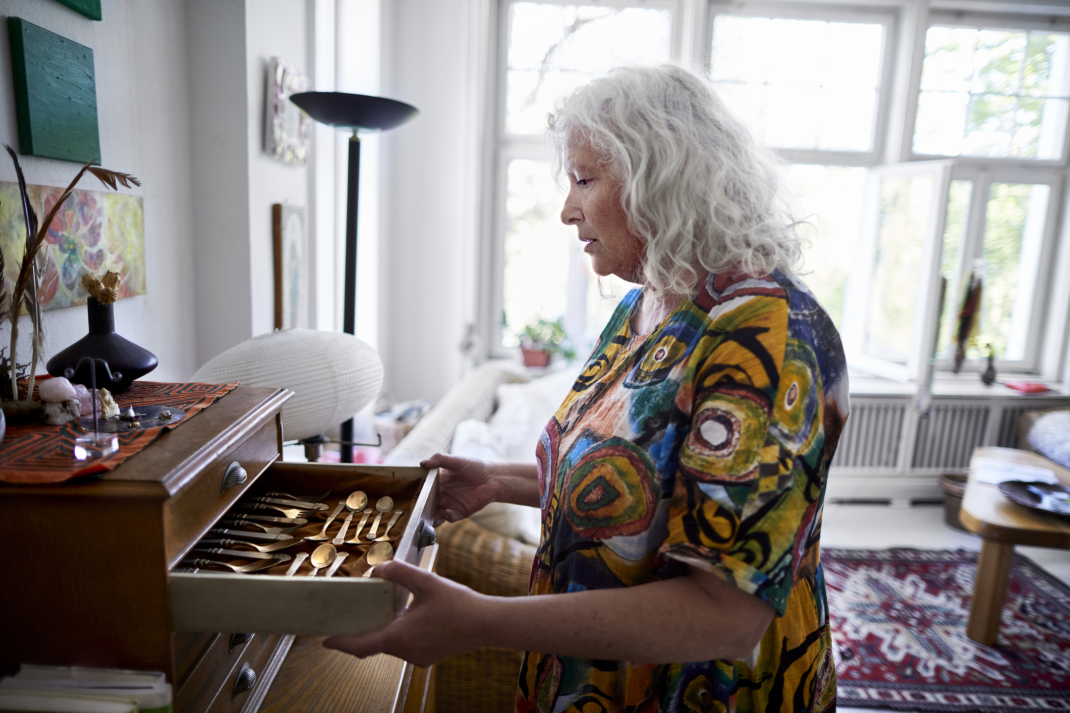 Senior woman wearing colorful at home opening drawer with precious cutlery