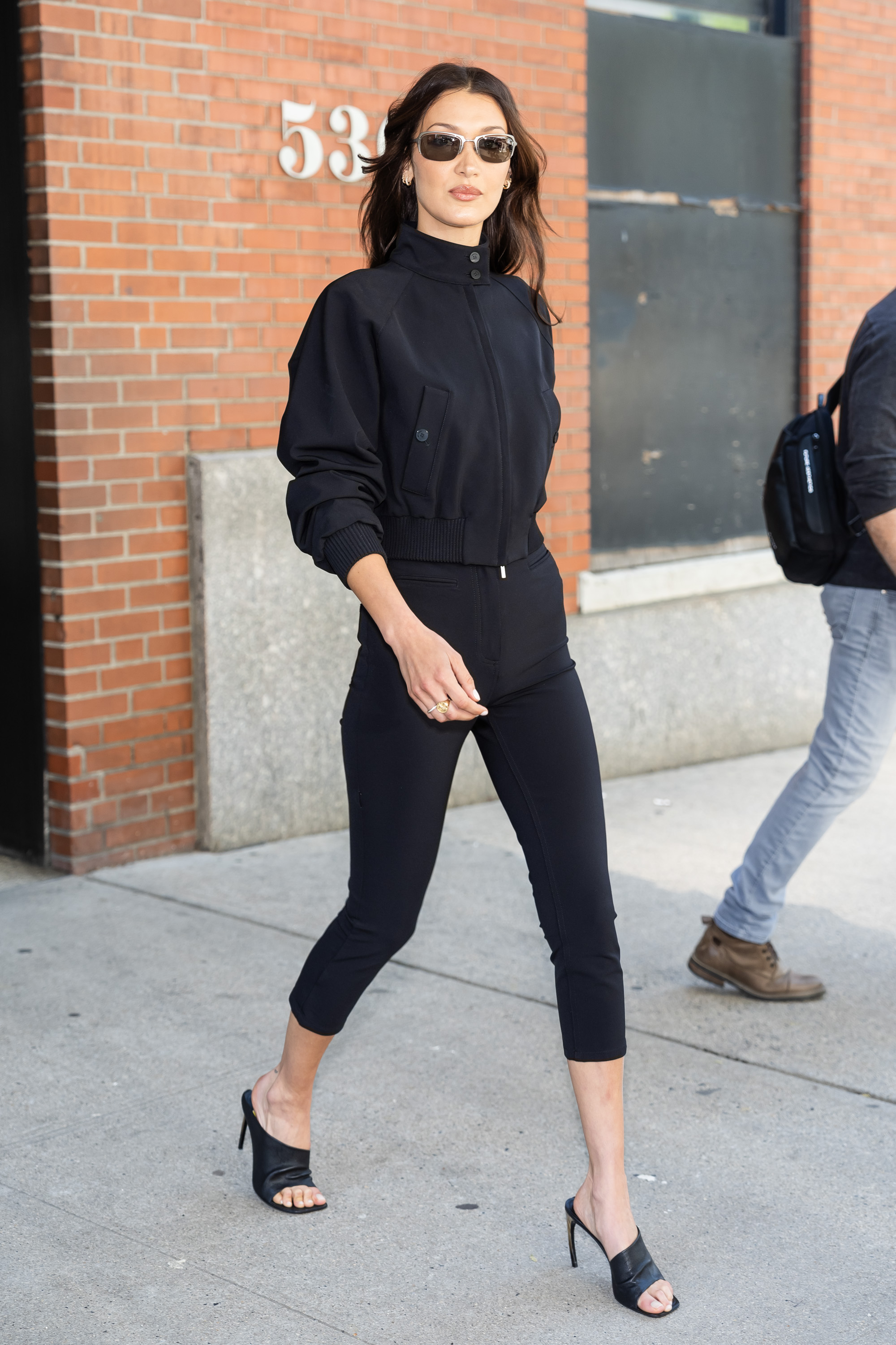 Bella Hadid in NYC wearing a black cropped jacket and black capri leggings with tall mules.