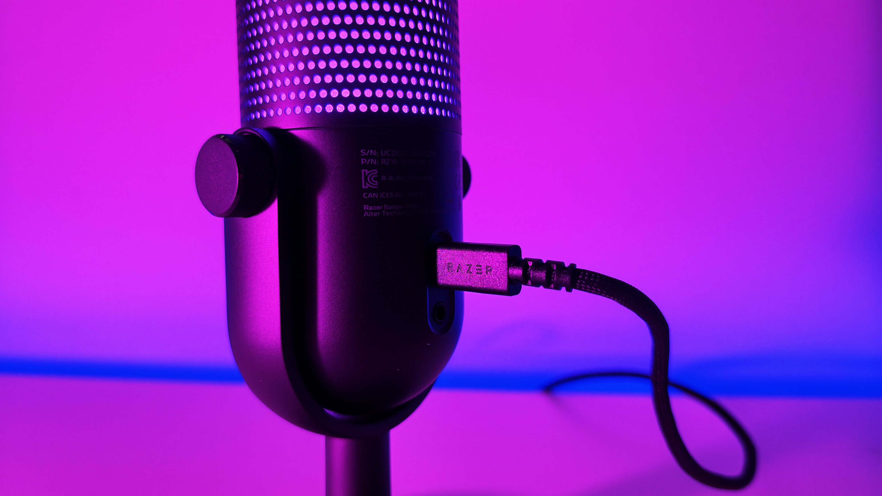 Close-up of the rear USB-C connection port on the Razer Seiren V3 Chroma microphone, shown under vibrant pink ambient light.