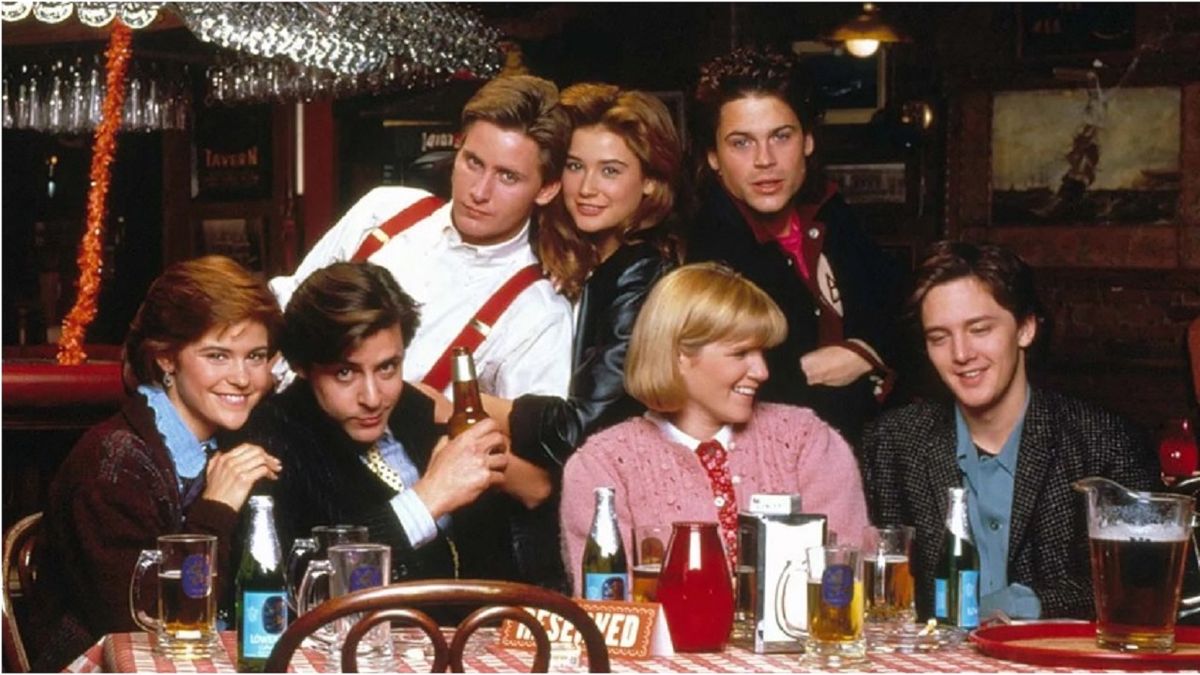 A 1980s image of the &#039;Brat Pack&#039; cast of &quot;St. Elmo&#039;s Fire&quot; gathered around a table in a bar