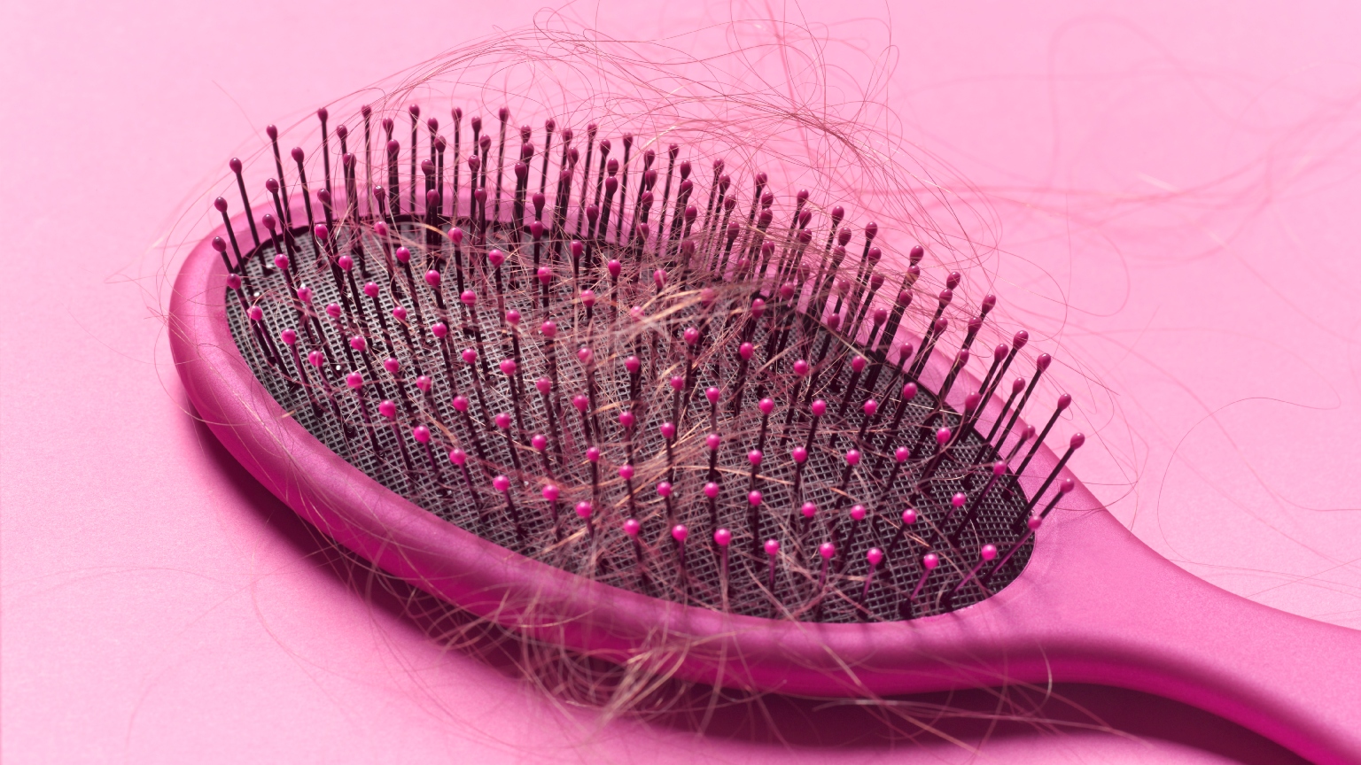 a pink hairbrush on a pink background with loose hairs