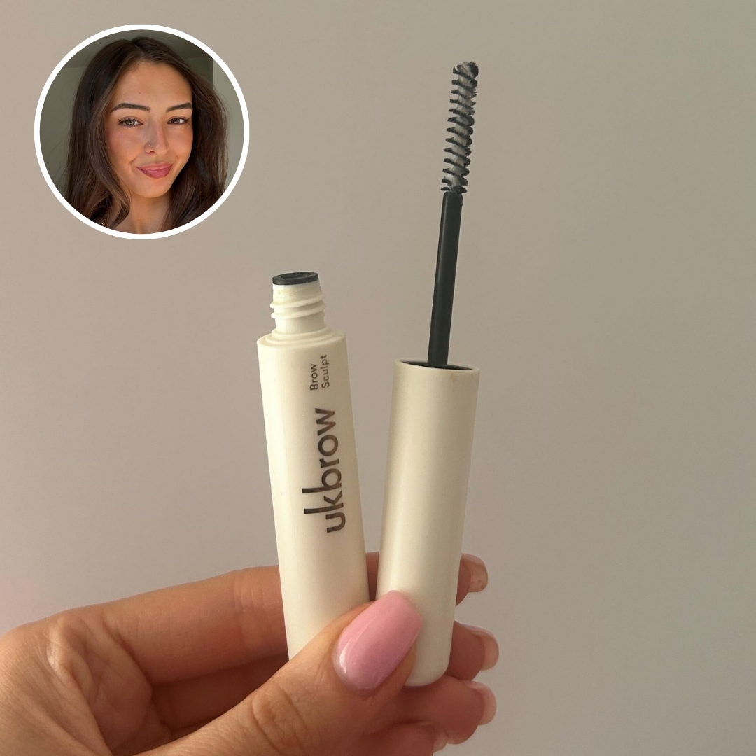 Hand holding an empty cream tube of UKLASH Brow Gel Sculpt, with circular photo of Sennen Prickett in top left corner