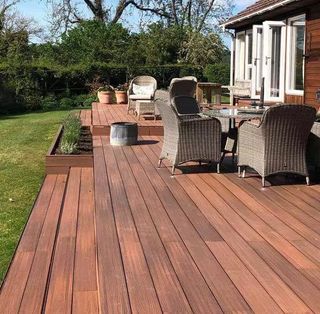 Natural wood finish composite decking in back garden with assortment of garden furniture
