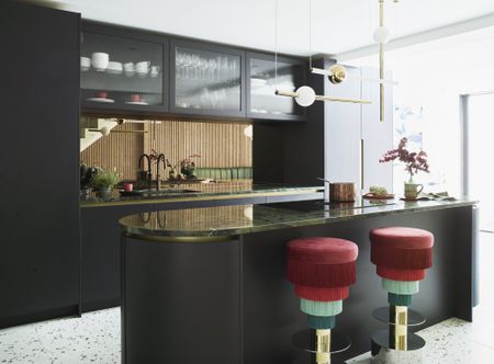 black kitchen with terrazzo flooring, gloss counterop, red and green fringed bar stools, retro pendant lights, curvy kitchen island 