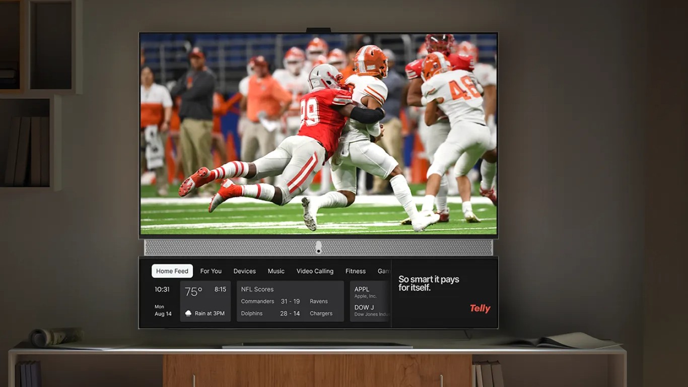 An image of a television displaying a scene from an American football game, with a secondary lower screen showing the time, date, various app categories (Home Feed, For You, Devices, Music, Video Calling, Fitness, Games), sports scores, stock information, and a Telly logo, with the text "So smart it pays for itself.".