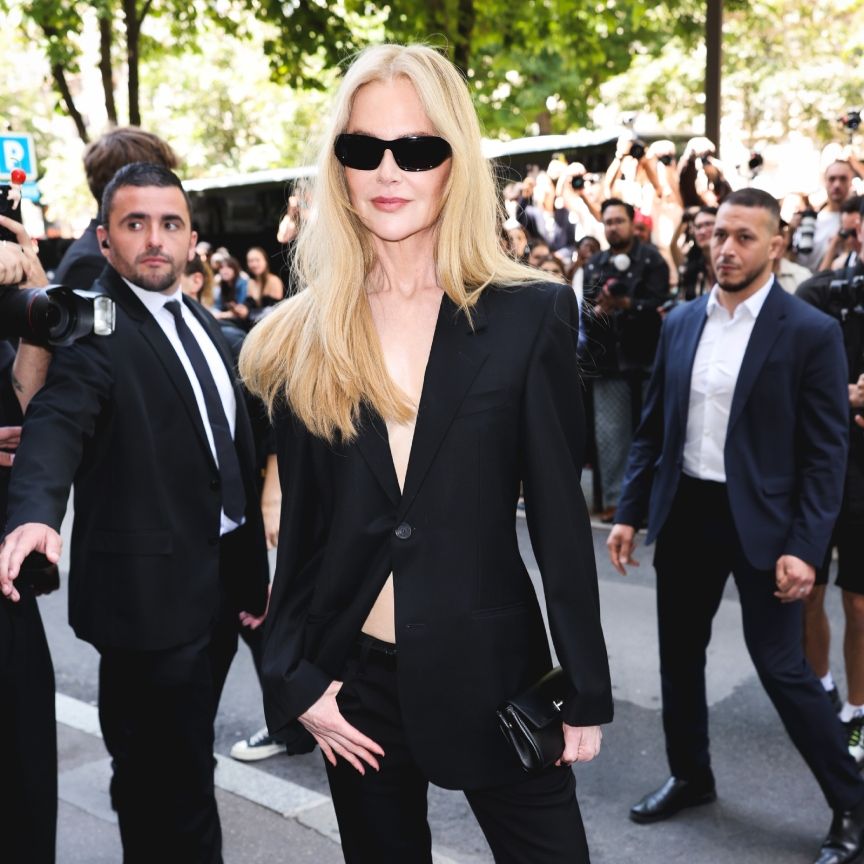 a white woman in a black jacket with sunglasses surrounded by photographers