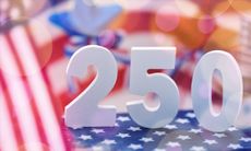 Large white numbers representing the 250th anniversary of the United States are displayed against a patriotic background of American flags and soft bokeh light.