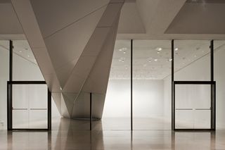 Front view of the lobby at the Rice Gallery. Beige tiles with white walls, and an asymmetrical white structure that comes down from the ceiling and touches the floor.