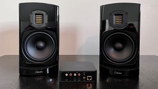 Schwarze Stereo-Lautsprecher auf einem schwarzen Tisch mit drahtlosem Streaming-Gerät.