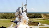 A white and blue rocket lifts off from a Florida launch pad during the day.