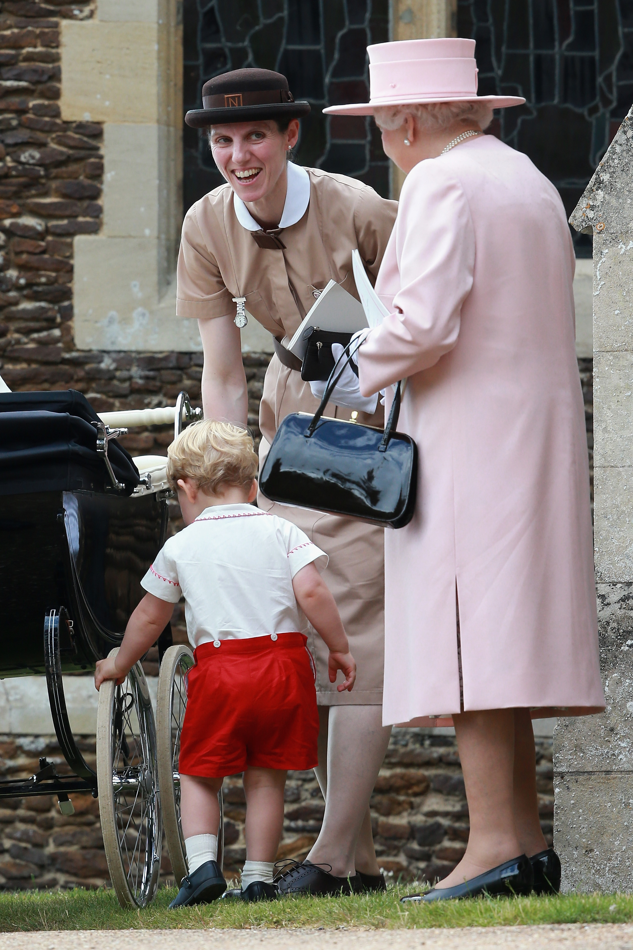 Prince George playing with the wheels of a stroller as Nanny Maria laughs with Queen Elizabeth