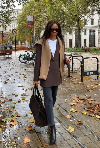 best black jeans is shown on a woman wearing a brown blazer over a white t-shirt with black straight-leg jeans, black ankle boots, and a brown handbag