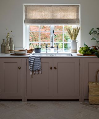 country kitchen with chalky pink cabinets, Portland Stone worktop, brick floor and neutral blind