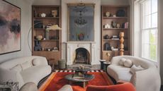 Living room with pale grey walls, white curved twin sofas, bright orange rug, black marble coffee table and wooden built-in shelving either side of a fireplace
