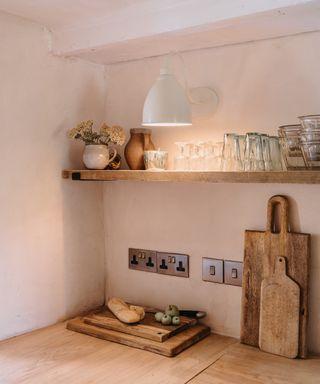 white metal wall light above wooden shelf with glasses and a wooden worktop with a series of wooden chopping boards