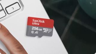 A SanDisk Ultra memory card sitting on a desk next to a laptop and its user's hand