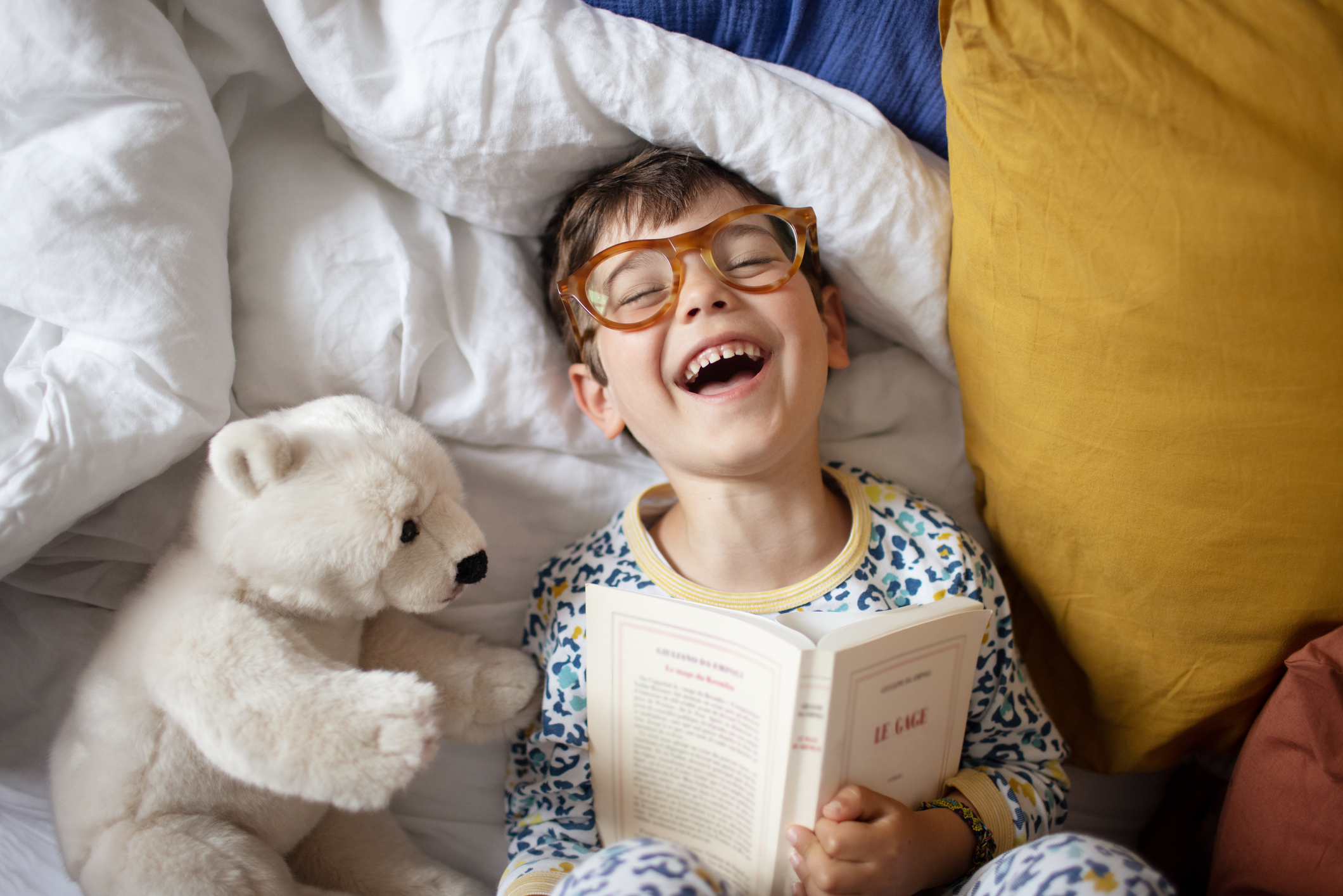 Portrait of a smiling little boy at home, he's wearing adult's glasses and pretending to read his parent's book