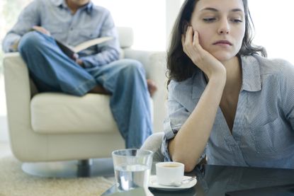 Woman leaning on elbow looking sad, man reading on sofa in background - what is a situationship
