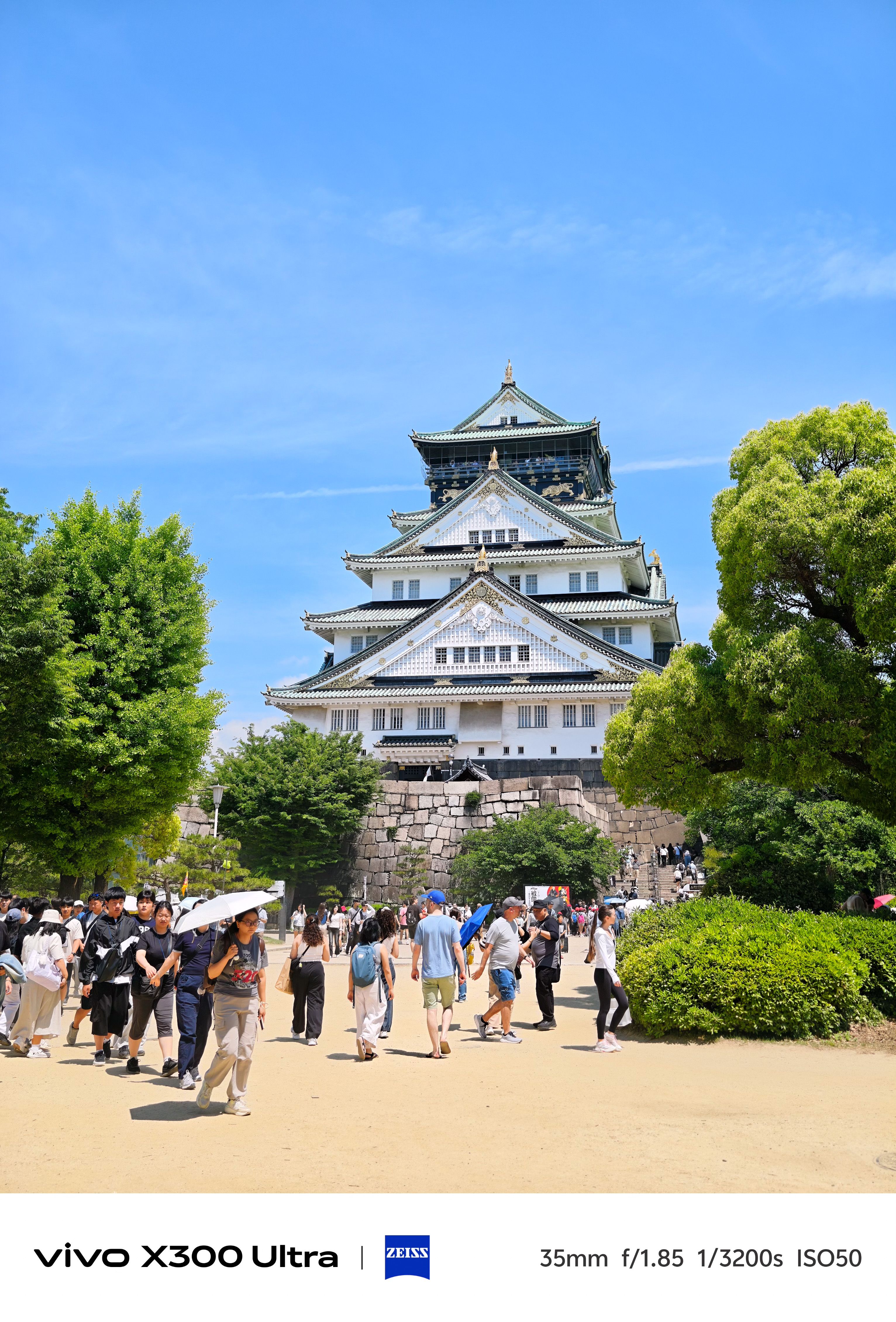 Osaka Castle framed by green trees under a clear blue sky, photographed on the Vivo X300 Ultra.