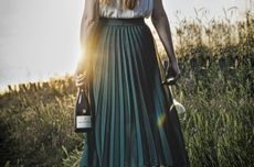 Woman walking through field holding bottle of Philipponnat, Royale R&eacute;serve Brut non-vintage Champagne