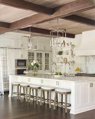 white kitchen with white island, bar stools, wooden floor, marble backsplash, chrome fixtures and fittings, glass cabinets
