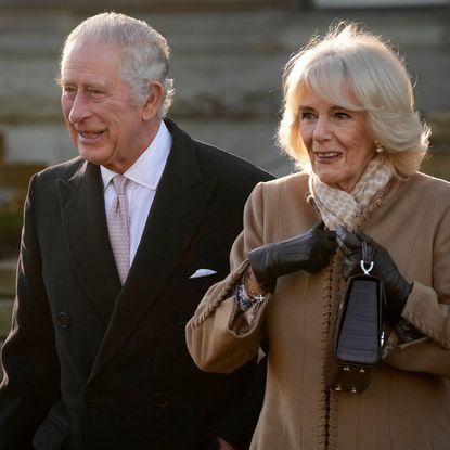 Queen Camilla and King Charles wearing coats standing next to each other outside and smiling