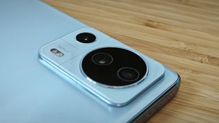 A light-blue Xiaomi 13 Lite camera phone sitting on a wooden desk