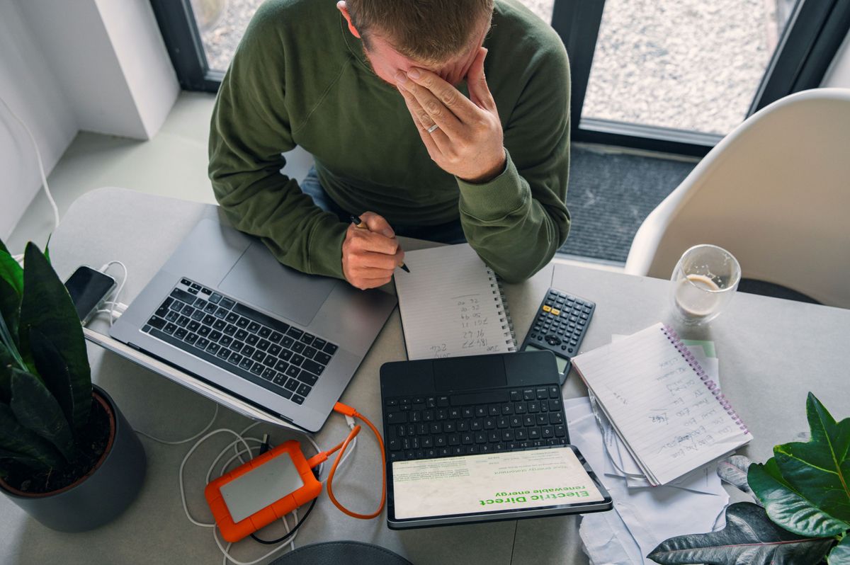 A man with his hand held to his head looks at his energy bills spread out on a table