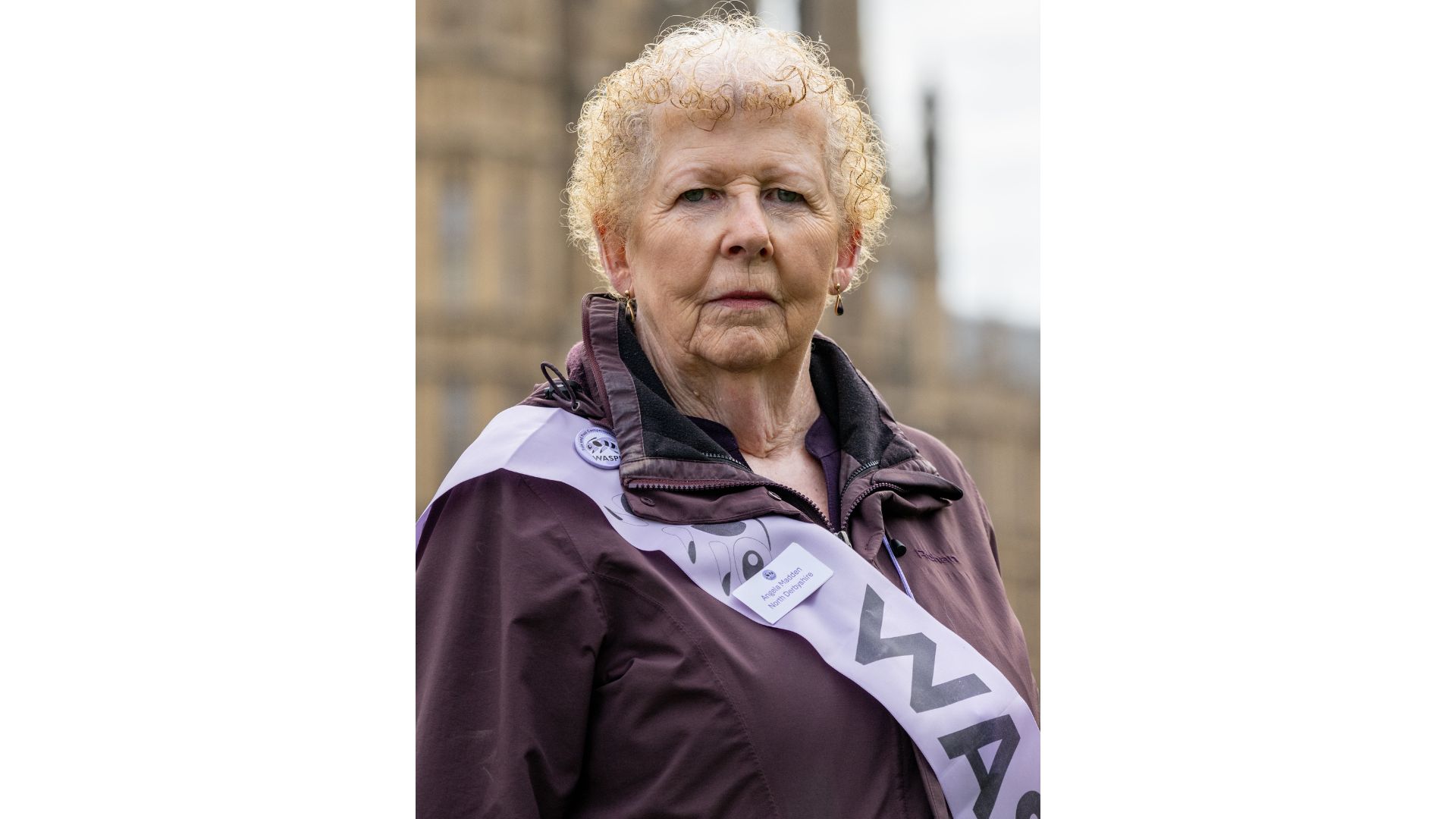 A headshot of Angela Madden, 71, campaigning outside UK parliament wearing a purple WASPI sash