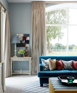 living room with neutral floor to ceiling curtains, pale blue walls and blue sofa