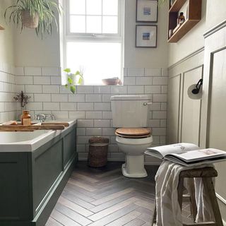a bathroom with a green/grey tub, glossy subway wall tiles, wood floors and plants