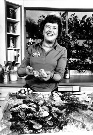 julia child holding up ingredients and smiling in a black and white photo from The French Chef