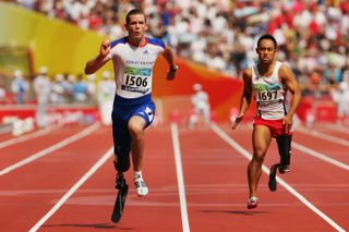 two athletes running at high speed down a lined track, with a crowd visible far in the back