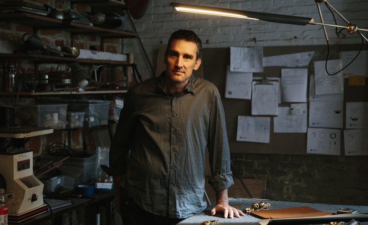 Designer David Weeks beneath the ‘Otto Two Arm Pendant’. Papers are pinned to a wall in the background