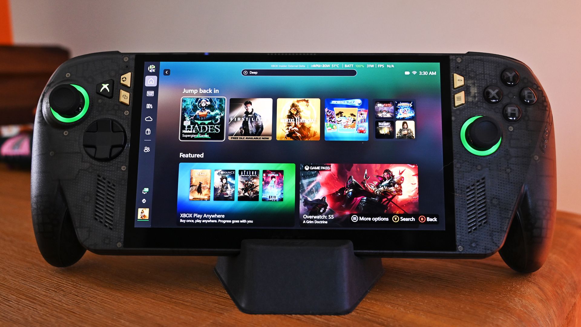 Front view of the ROG Ally X20 handheld resting on a desk dock, showing the Xbox dashboard game tiles and illuminated green joystick rings.