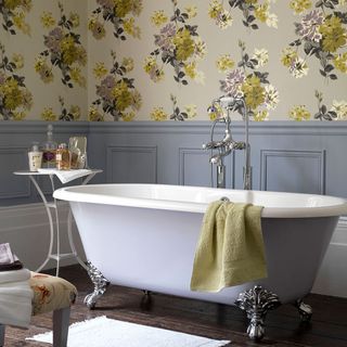 bathroom with yellow flower wall bathtub with towel and wooden flooring