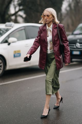 a woman at milan fashion week wearing a burgundy blazer with an olive green skirt and black pumps