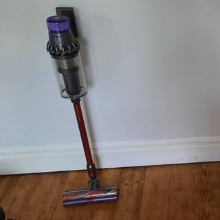 Dyson cordless vacuum cleaner stored upright against wall