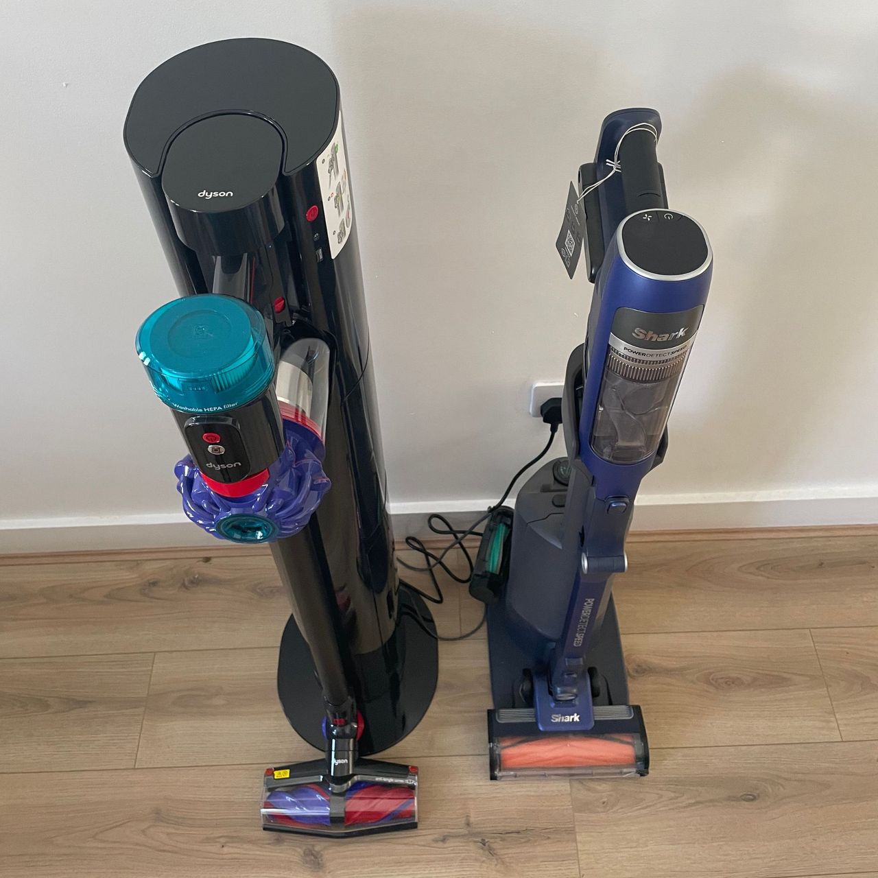 Dyson V10 Konical and auto-empty dok standing next to the Shark PowerDetect speed on wood-effect flooring