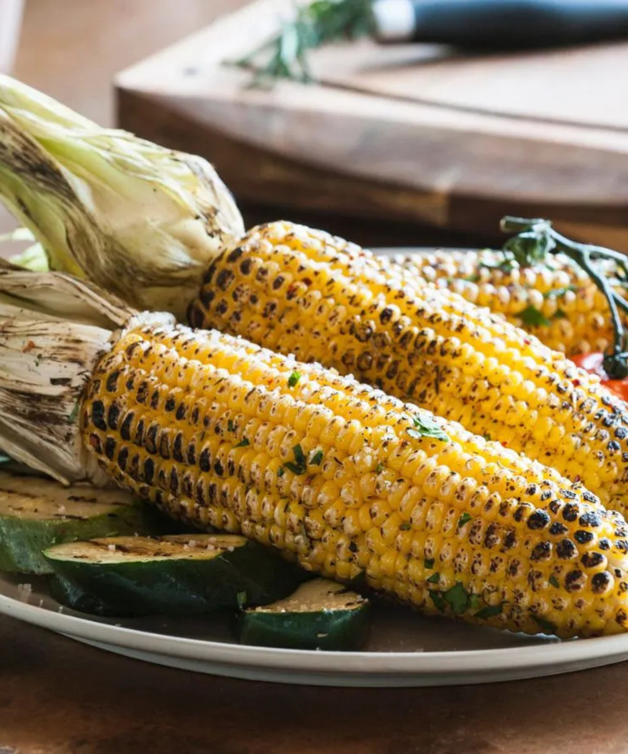 A plate of corn grilled in the jusk with zucchini and tomatoes