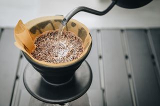 Close up of barista pouring hot water on ground coffee with paper filter to making a drip coffee