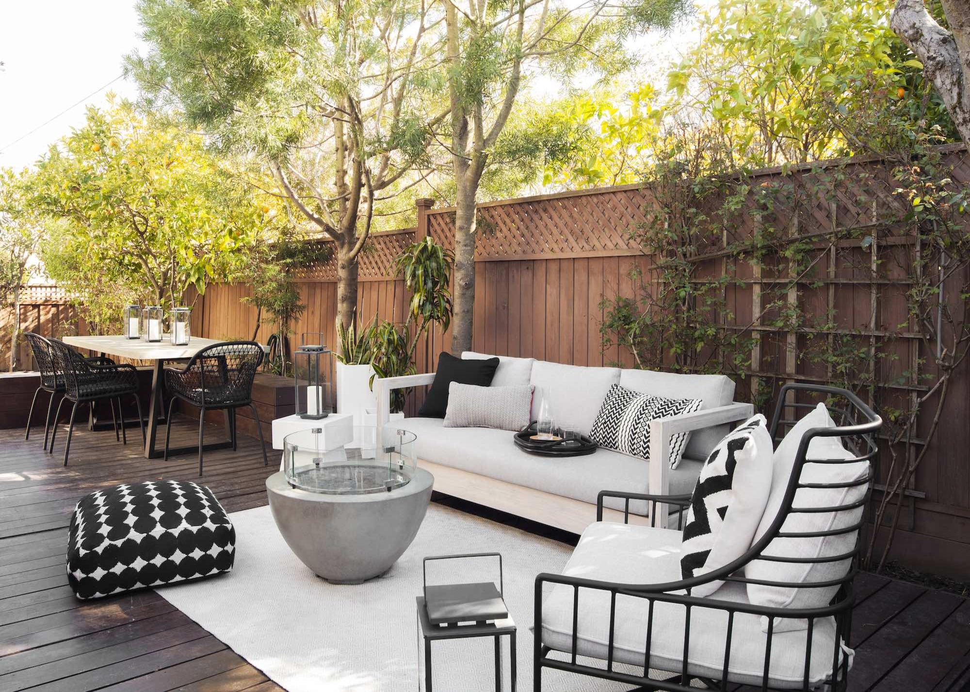 A decking area with black and white garden furniture in the foreground and a wooden dining table in the background