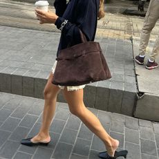 Annelaure Mais wearing a white miniskirt with black heeled mules and carrying a brown suede tote bag.