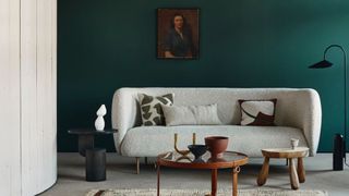 A forest green wall with a neutral sofa sat against it illustrating the forest green color trend