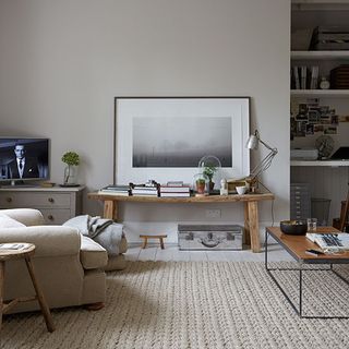 living room with white wall painting on wooden desk cream colour sofa chair and white shelf on wall