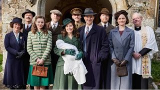 The cast of All Creatures Great and Small in front of a child and with Helen Herriot (played by Rachel Shenton) holding baby James in a promo shot for All Creatures Great and Small season 5