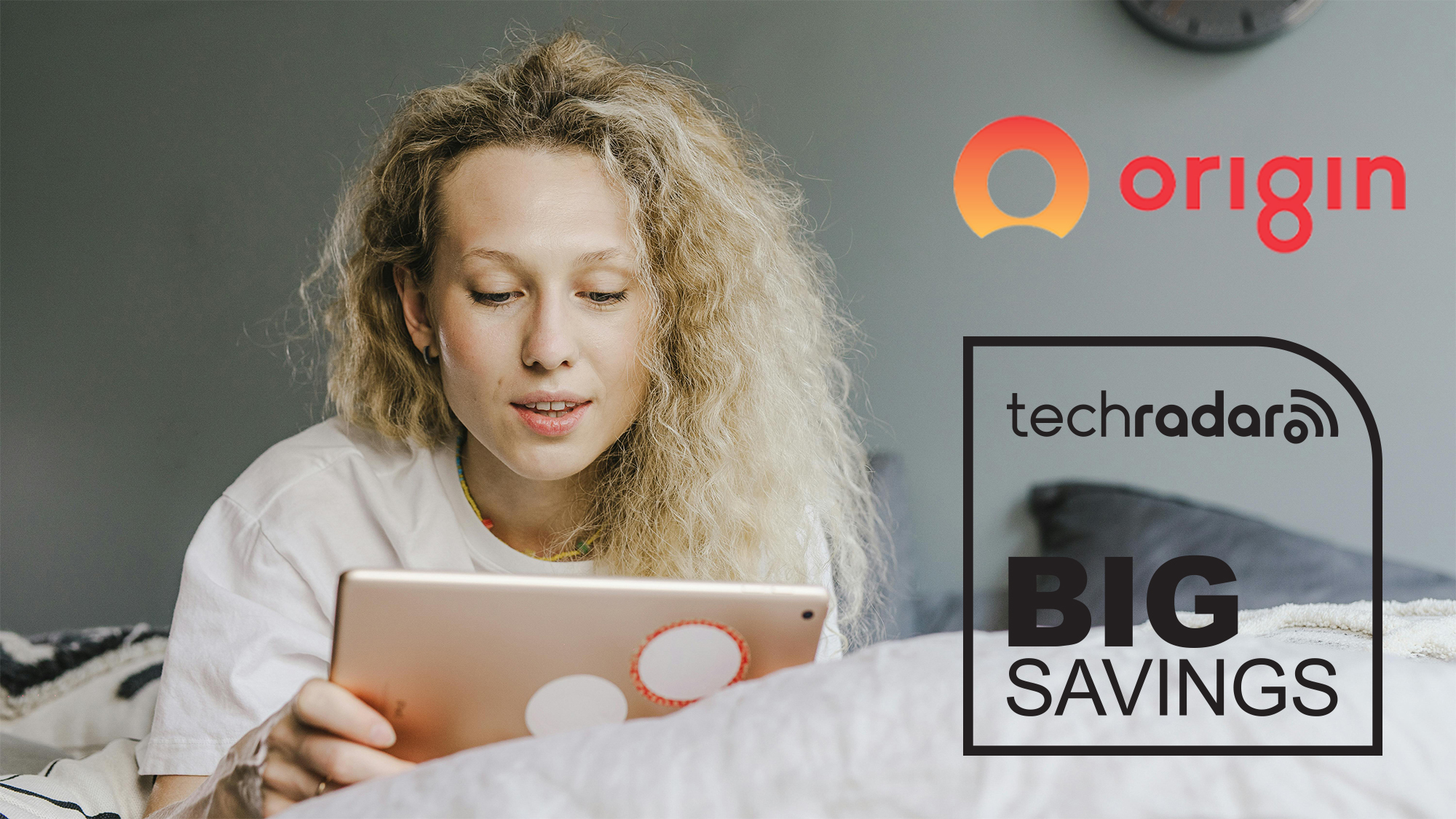 A young woman lying on her front looking at a tablet computer that she is holding in her right hand. The Origin Energy and TechRadar 'Big Savings' logos sit overlaid on the right side of the image.
