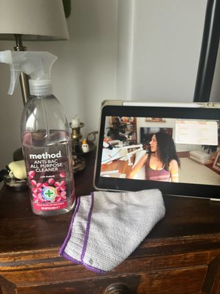 A bottle of pink method cleaning spray on a night stand beside an Ipad and a microfiber clenaing cloth